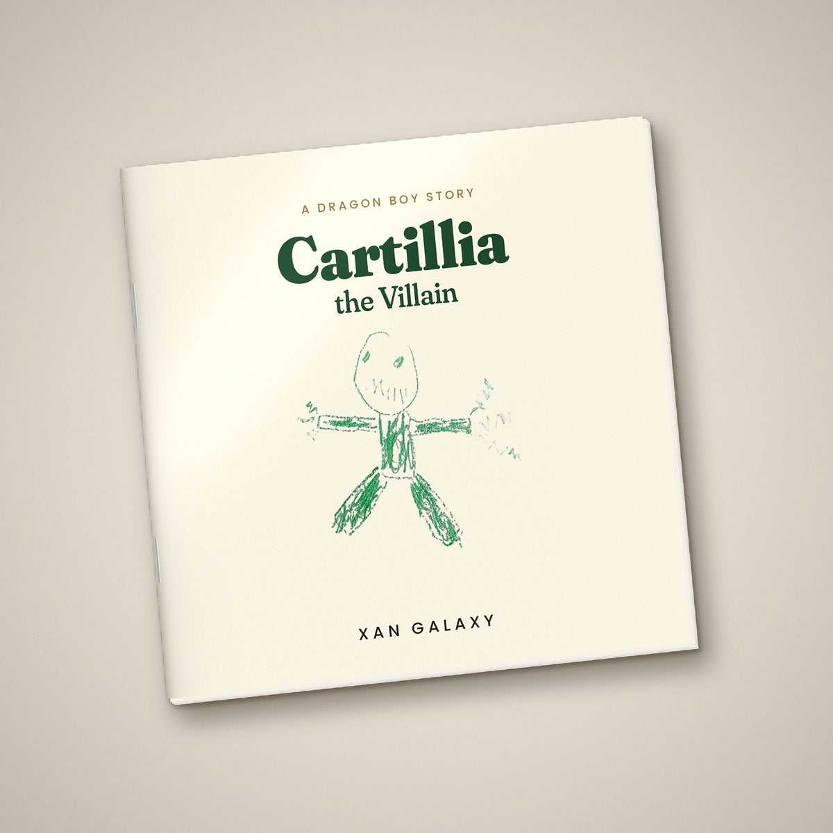 Sample As Drawn paperback lying on a table, a square printed picture book with a child's green crayon villain on the cover